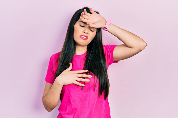 Jong Latijns-Amerikaans meisje draagt casual roze t-shirt aanraken voorhoofd voor ziekte en koorts, griep en kou, virus ziek  - Foto, afbeelding