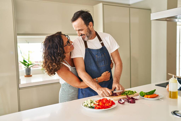 Middle age hispanic couple smiling confident and hugging each other cooking at kitchen - Photo, Image
