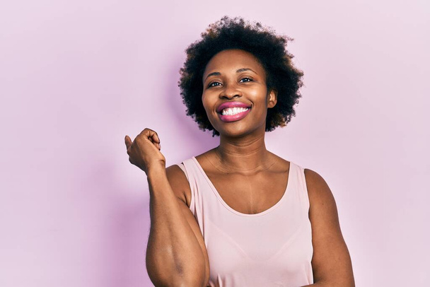 Young african american woman wearing casual sleeveless t shirt with a big smile on face, pointing with hand and finger to the side looking at the camera.  - Photo, Image