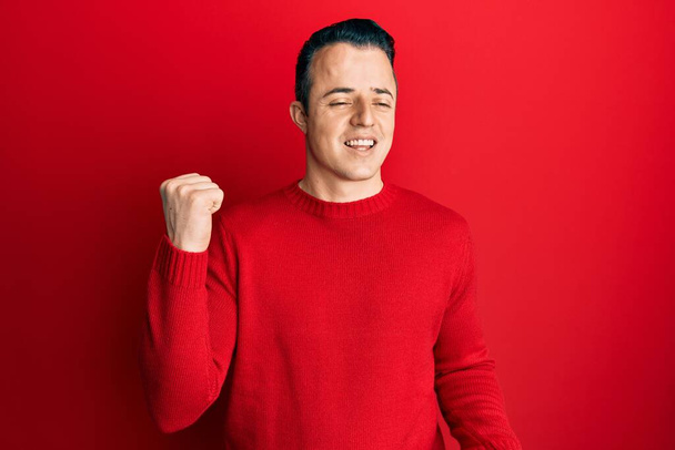 Handsome young man wearing casual winter sweater celebrating surprised and amazed for success with arms raised and eyes closed  - 写真・画像