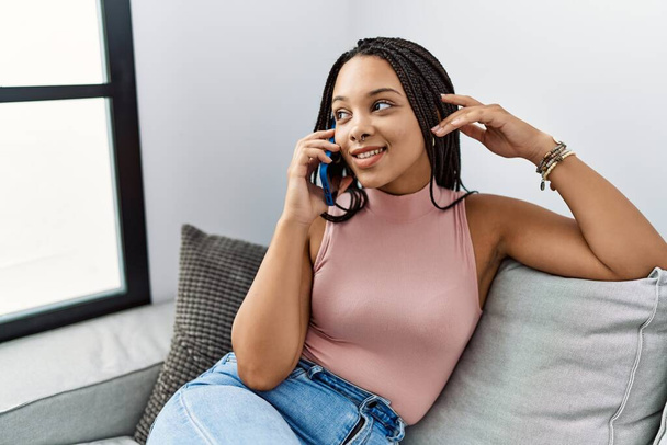 Jovem afro-americana sorrindo confiante falando no smartphone em casa - Foto, Imagem