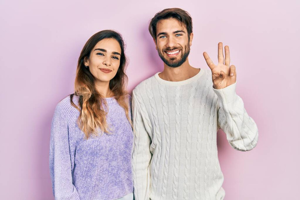 Молода пара іспаномовних носить повсякденний одяг, показуючи і вказуючи пальцями номер три, посміхаючись впевнено і щасливо
.  - Фото, зображення