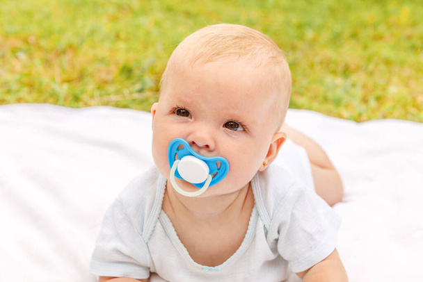 Cute little newborn girl lying on tummy on blanket in lawn on sunny summer day outdoor. Infant having fun outdoors. Infant baby child resting playing learning to crawl. Motherhood happy child concept. - Photo, Image