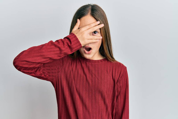 Bella ragazza bruna che indossa maglione casual sbirciando in shock che copre il viso e gli occhi con la mano, guardando attraverso le dita impaurite  - Foto, immagini