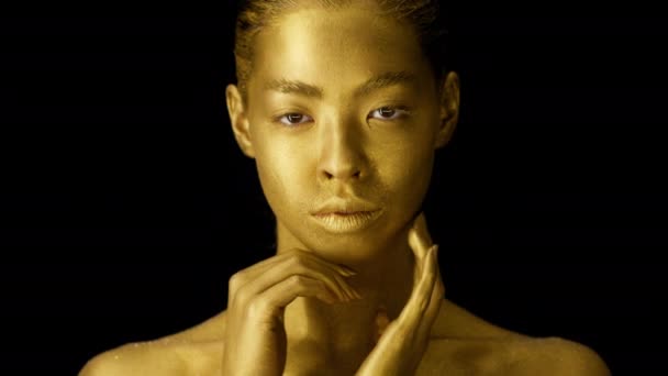 Жінка з золотою шкірою позує торкаючись обличчя над чорним тлом
 - Кадри, відео