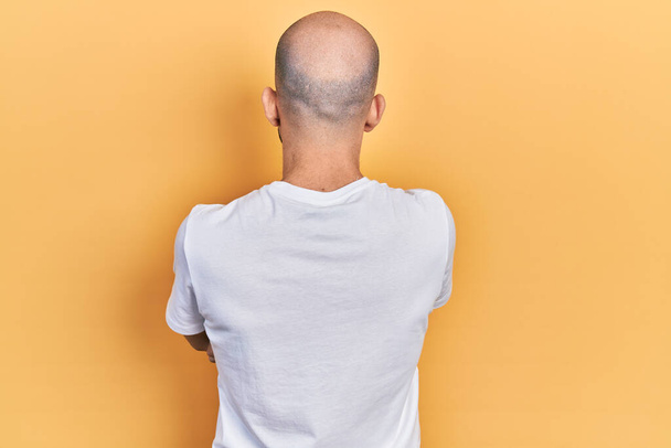 Young bald man wearing casual white t shirt standing backwards looking away with crossed arms  - Photo, Image