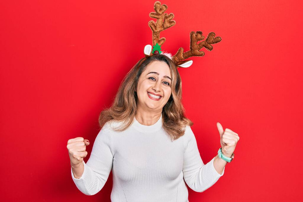 Middle age caucasian woman wearing cute christmas reindeer horns excited for success with arms raised and eyes closed celebrating victory smiling. winner concept.  - Photo, Image