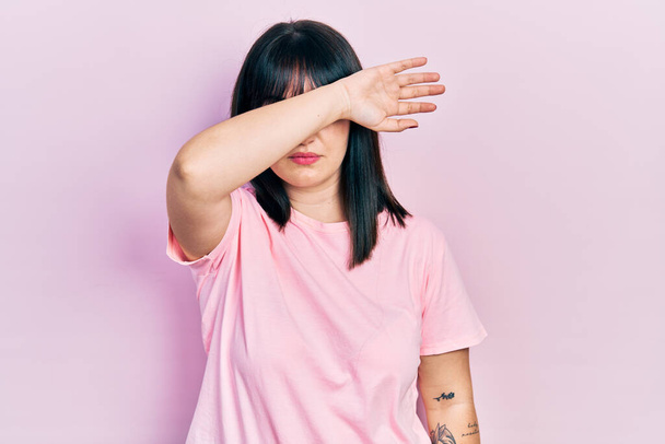 Young hispanic woman wearing casual clothes covering eyes with arm, looking serious and sad. sightless, hiding and rejection concept  - Photo, Image