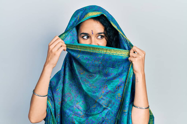 Young indian woman wearing sari covering head and face, doing elegant pose with traditional scarf - Zdjęcie, obraz