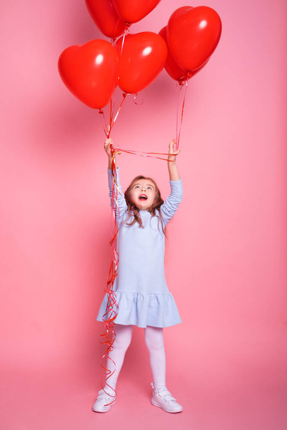 Beautiful child girl with red heart romantic balloons on pink background. Concept of Valentines day - Foto, Imagem