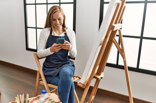 若い白人女性が自信を持って笑顔でスマートフォンを使ってアートスタジオ - 写真・画像