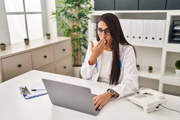 Young hispanic doctor woman doing video call at the clinic covering mouth with hand, shocked and afraid for mistake. surprised expression  - Photo, Image
