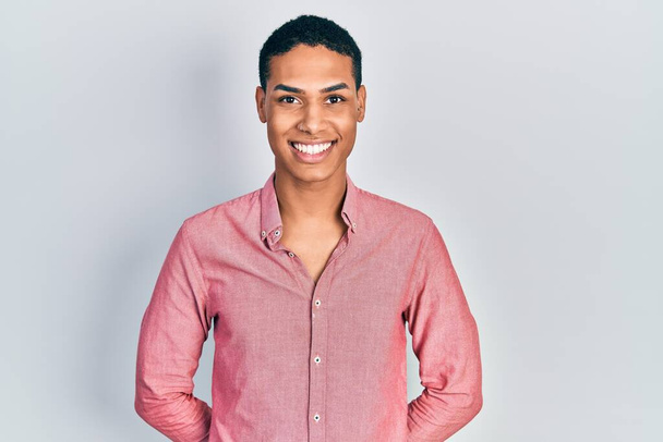 Jeune homme afro-américain portant des vêtements décontractés regardant positif et heureux debout et souriant avec un sourire confiant montrant les dents  - Photo, image