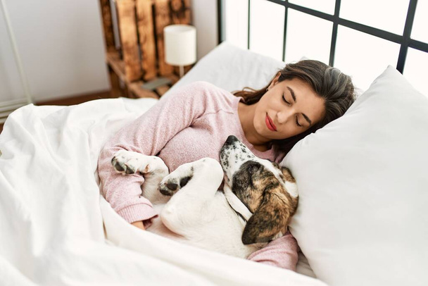 Νεαρή γυναίκα κοιμάται ξαπλωμένη στο κρεβάτι με το σκύλο στο υπνοδωμάτιο - Φωτογραφία, εικόνα
