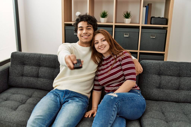Giovane coppia sorridente felice guardando la tv seduta sul divano a casa. - Foto, immagini