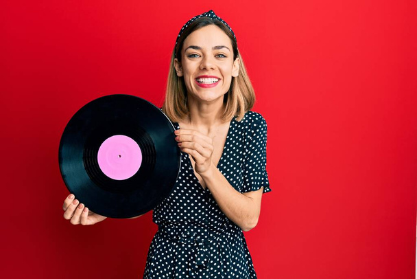 Young caucasian blonde woman holding vinyl disc smiling and laughing hard out loud because funny crazy joke.  - Photo, Image