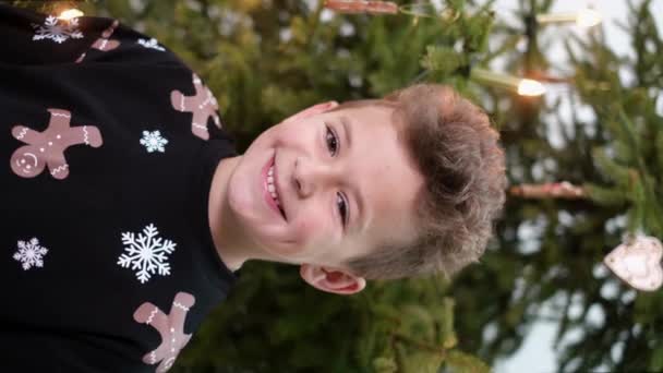 Glückliches Kind blickt in die Kamera auf dem Hintergrund des Weihnachtsbaums.  - Filmmaterial, Video
