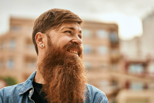 Joven irlandés hipster hombre sonriendo feliz de pie en la ciudad. - Foto, Imagen