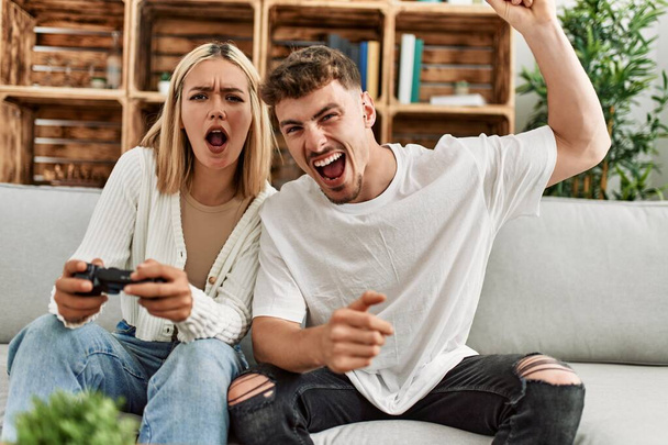 Νεαρό καυκάσιο ζευγάρι ουρλιάζοντας παίζοντας βιντεοπαιχνίδι στο σπίτι. - Φωτογραφία, εικόνα