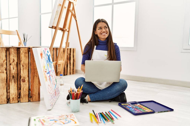 Молодая женщина с ноутбуком, сидящая на полу в художественной студии - Фото, изображение