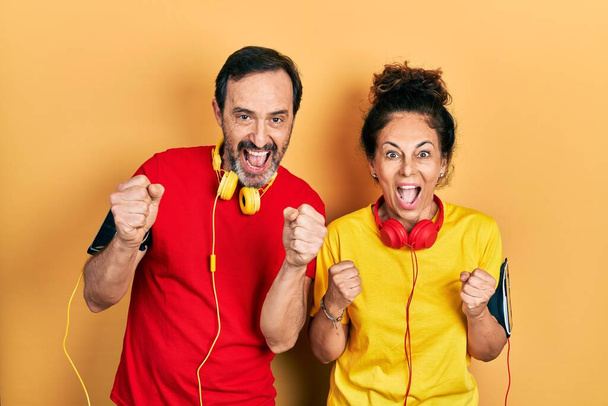 Middle age couple of hispanic woman and man wearing sportswear and arm band celebrating surprised and amazed for success with arms raised and open eyes. winner concept.  - Photo, Image