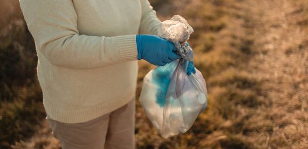 Earth day. Female activist hand puts a plastic bottle trash in a garbage bag. - 写真・画像