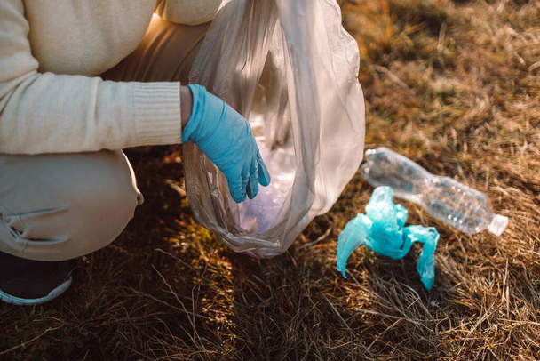 Earth day. Female activist hand puts a plastic trash in a garbage bag. Earth planet dirty and polluted. Environmental protection and waste reduction. - Foto, Imagem