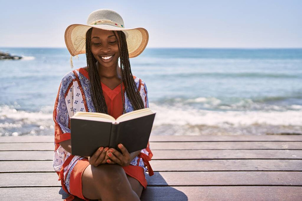 Junge afrikanisch-amerikanische Frau liest Buch auf der Bank am Strand. - Foto, Bild