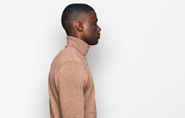 Jonge Afrikaanse Amerikaanse man draagt casual winter trui op zoek naar kant, ontspannen profiel poseren met een natuurlijk gezicht met een zelfverzekerde glimlach.  - Foto, afbeelding