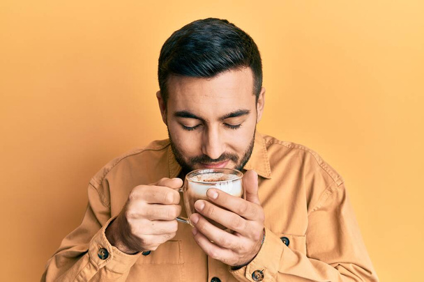 Красивый латиноамериканец наслаждается чашкой кофе на жёлтом фоне - Фото, изображение