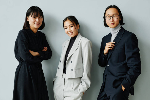 Cintura hacia arriba retrato de un moderno equipo de negocios asiático sonriendo a la cámara de pie sobre un fondo mínimo - Foto, Imagen
