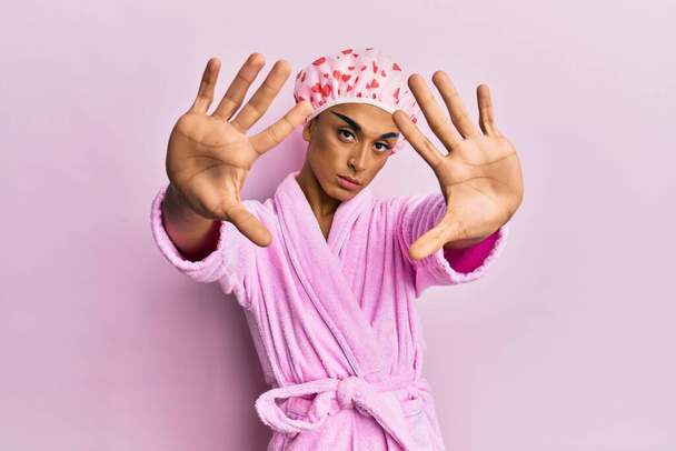 Hispanic man wearing make up wearing shower towel cap and bathrobe doing frame using hands palms and fingers, camera perspective  - Photo, Image
