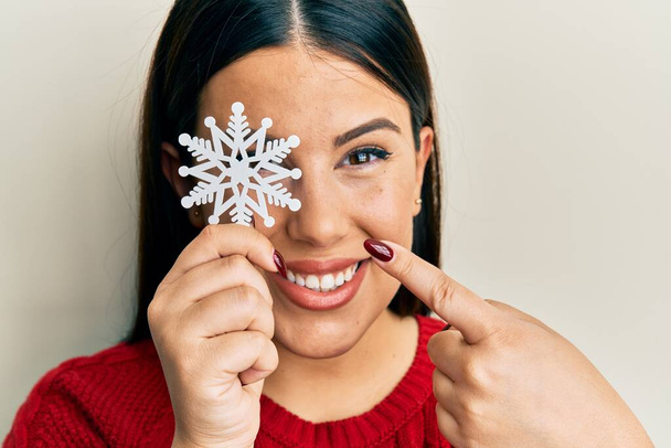 Bella donna bruna che tiene il fiocco di neve sopra l'occhio sorridente felice indicando con mano e dito  - Foto, immagini
