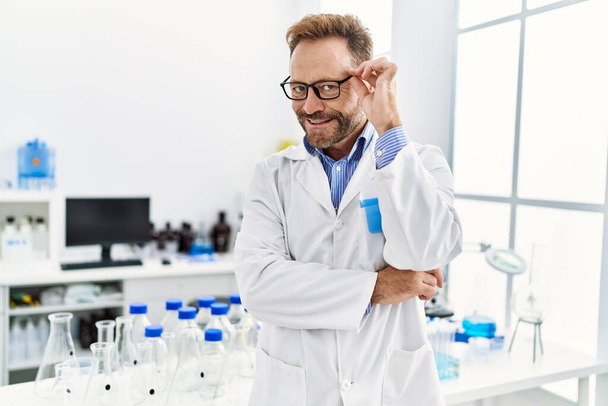 Hispanischer Mann mittleren Alters in Wissenschaftleruniform steht im Labor - Foto, Bild