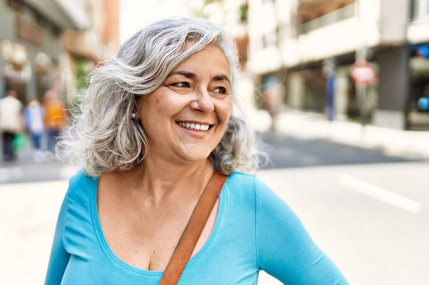 Orta yaşlı, kır saçlı, gülümseyen bir kadın şehirde mutlu mesut duruyor.. - Fotoğraf, Görsel