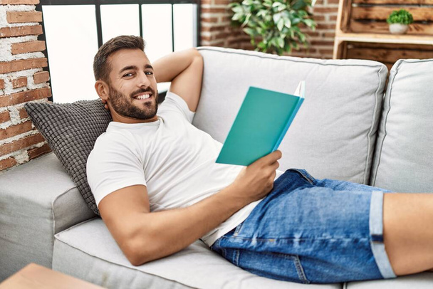 Jeune homme hispanique souriant livre de lecture confiant à la maison - Photo, image