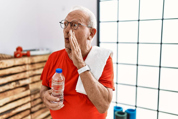 Vanhempi mies yllään urheiluvaatteet ja pyyhe kuntosalilla käsi suulla kertoo salaisia huhuja, kuiskaa ilkeä puhua keskustelu  - Valokuva, kuva