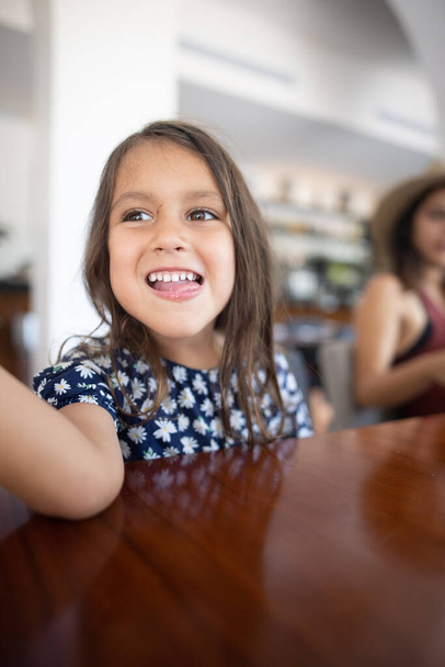 Милая маленькая девочка сидит за столом ресторана с расплывчатым фоном - Фото, изображение