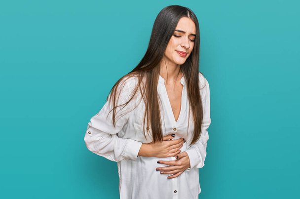 Young beautiful woman wearing casual white shirt with hand on stomach because indigestion, painful illness feeling unwell. ache concept.  - Photo, Image