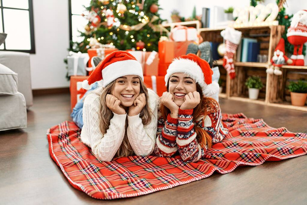 Frauenpaar lächelt zuversichtlich auf dem Boden liegend bei Weihnachtsdekoration zu Hause - Foto, Bild