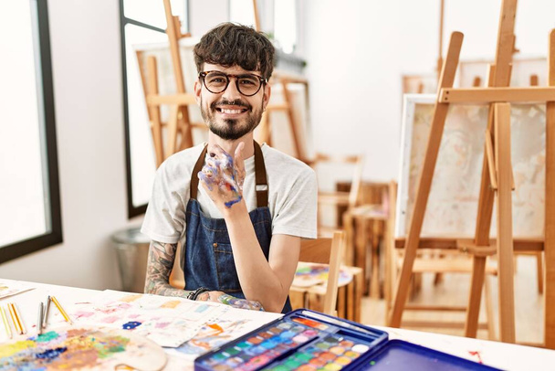 Латиноамериканець з бородою на художній студії з упевненістю дивиться на камеру, посміхаючись перехрещеними руками і руками, вирощеними на підборідді. позитивне мислення.  - Фото, зображення