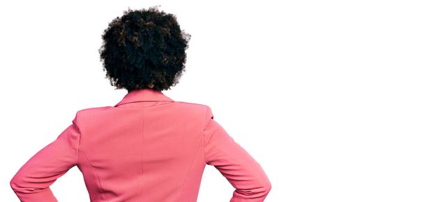 Африканська американка з волоссям афроамериканського кольору, одягнена в ділову куртку, стоїть ззаду, дивлячись з руками на тіло.  - Фото, зображення