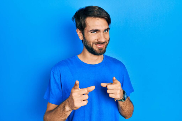 Junger hispanischer Mann in lässiger Kleidung, der mit erhobenem Zeigefinger in die Kamera zeigt, mit fröhlichem und lustigem Gesicht. gute Energie und Stimmung.  - Foto, Bild