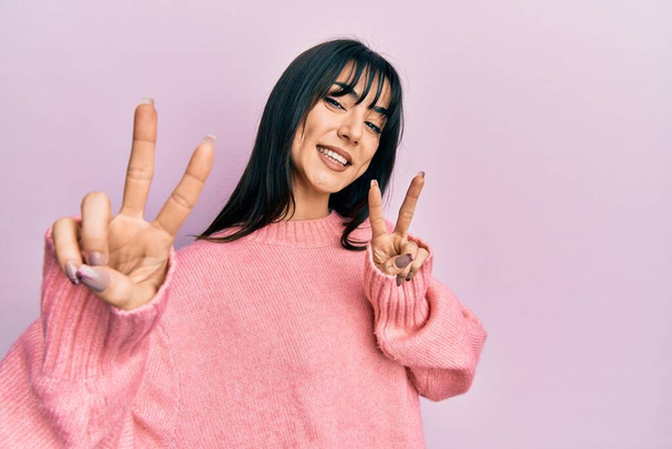 Young brunette woman with bangs wearing casual winter sweater smiling looking to the camera showing fingers doing victory sign. number two.  - Photo, Image