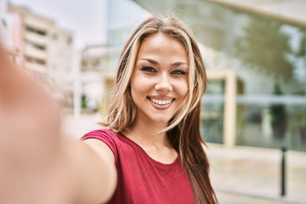 Joven chica caucásica sonriendo feliz haciendo selfie por la cámara en la ciudad. - Foto, Imagen