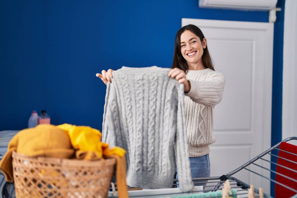 Молодая женщина улыбается уверенно висит одежду на веревке в прачечной - Фото, изображение