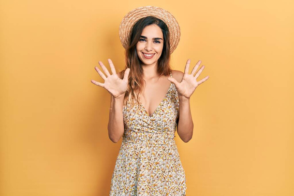 Mladá hispánská dívka v letním klobouku ukazuje a ukazuje prsty číslo deset a přitom se usmívá sebevědomě a šťastně.  - Fotografie, Obrázek