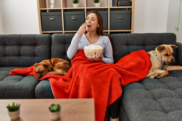 Young hispanic woman watching movie sitting on sofa with dogs at home - Fotó, kép