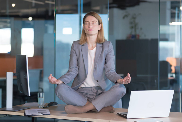 Business woman alone sitting at desk in her office, female employee meditating in lotus position - Fotó, kép