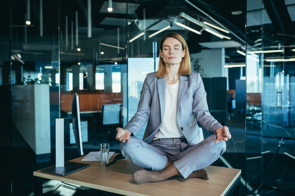 Biznes kobieta sama siedzi przy biurku w swoim biurze, kobieta pracownik medytuje w pozycji lotosu - Zdjęcie, obraz
